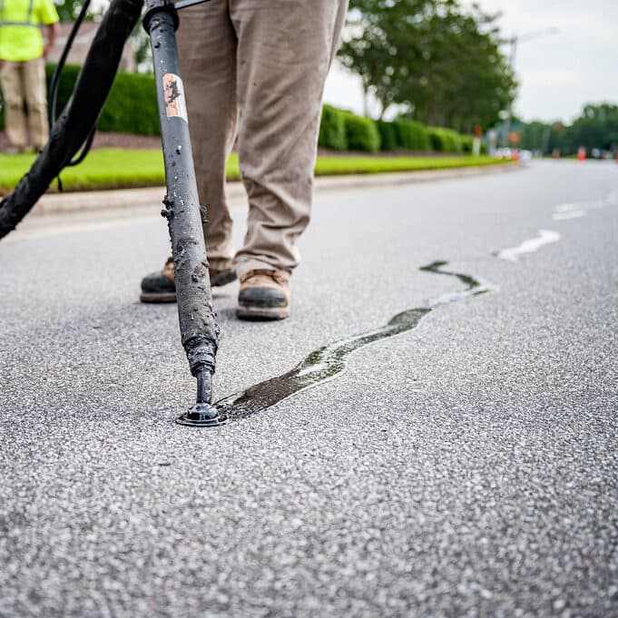 Crack sealant wand running hot rubber along a pavement crack