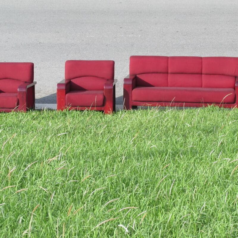 A red sofa and two matching armchairs set out on the grass at the curb