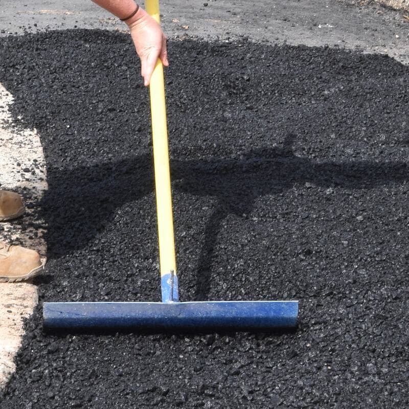A lute spreading fresh hot mix asphalt into a parking lot patch