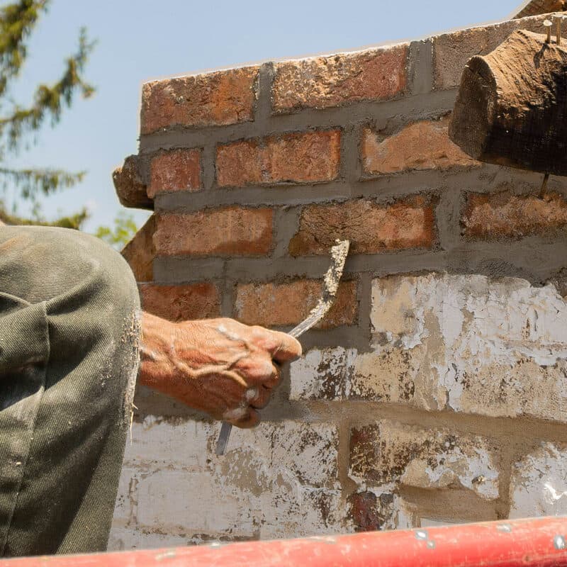 A mason presses fresh mortar into the joints of a brick chimney with a pointing tool