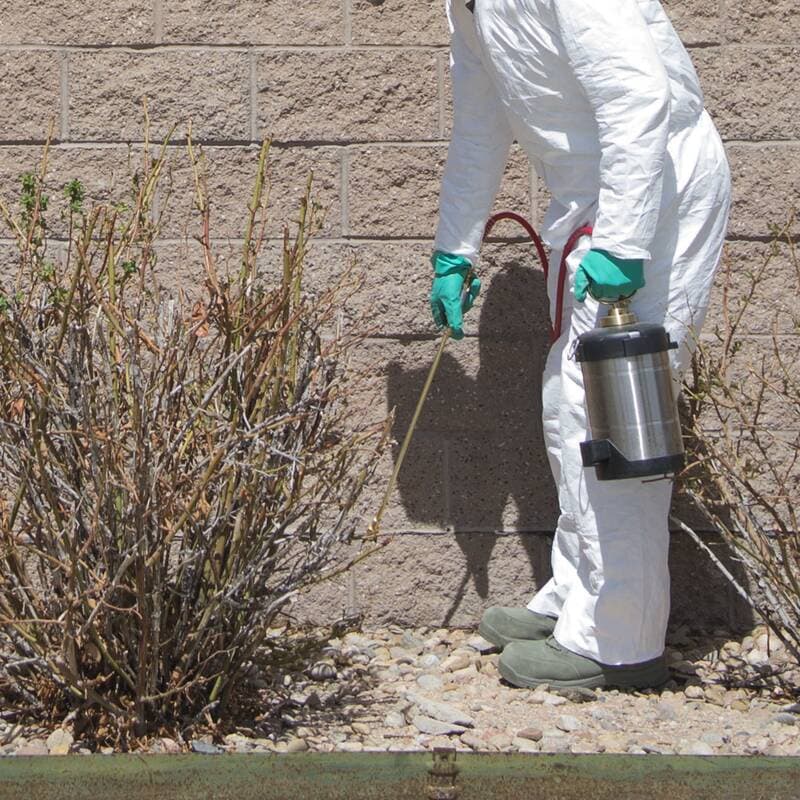 A pest control technician sprays along the foundation of a building
