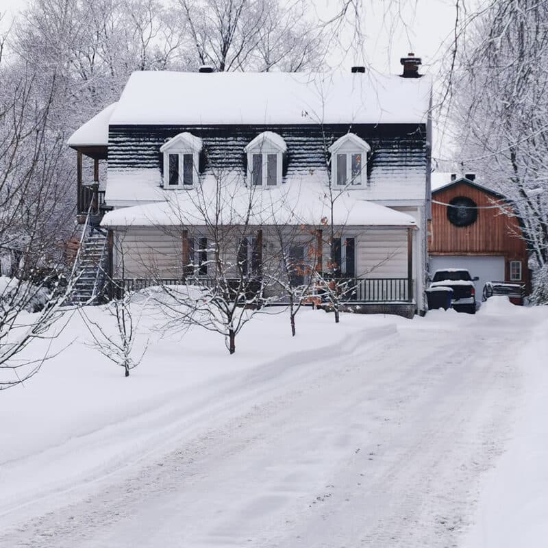 A plowed driveway running up to a closed garage door with snow piled along the edge