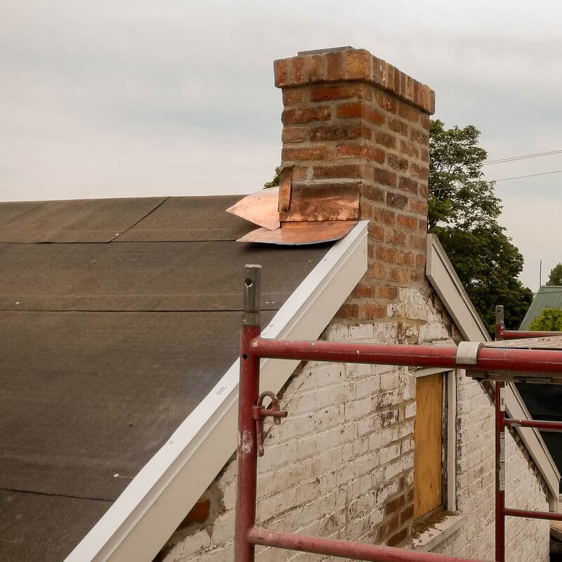 Copper flashing at the base of a brick chimney, seen from a scaffold at the roof edge