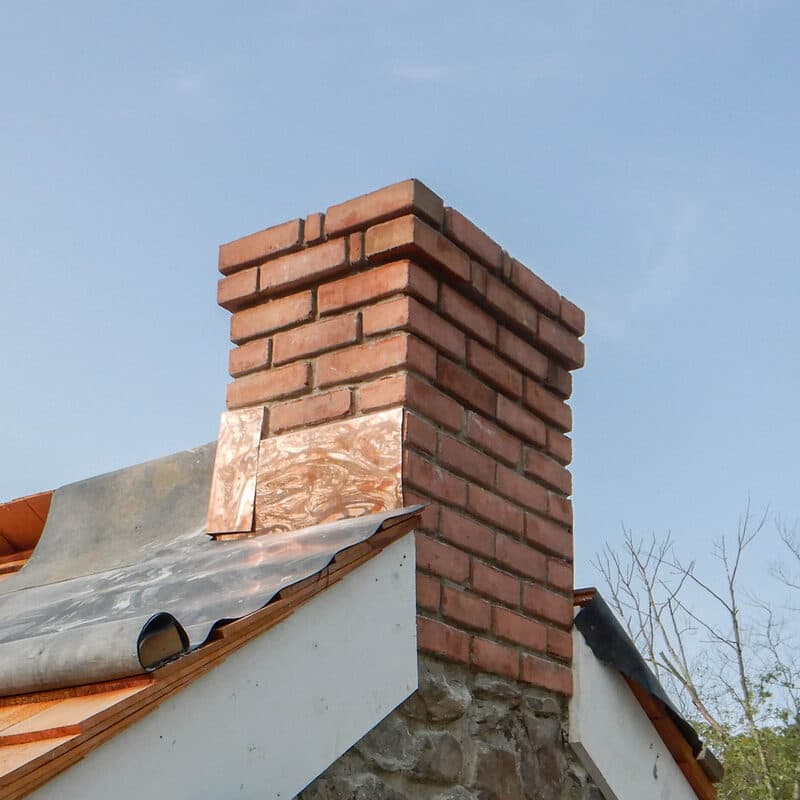 A rebuilt brick chimney top with new copper flashing against a clear sky