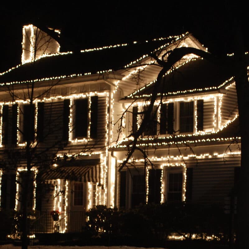 A two story house at night with warm lights outlining the roofline, windows and dormer