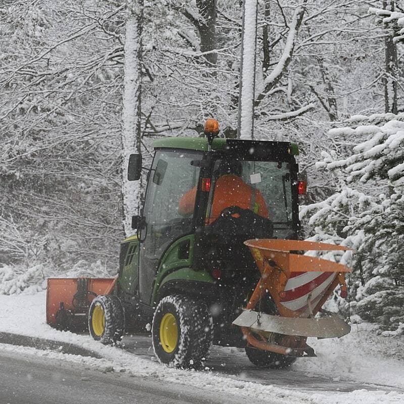 Compact tractor with a front plow and a rear salt spreader on a snowy road