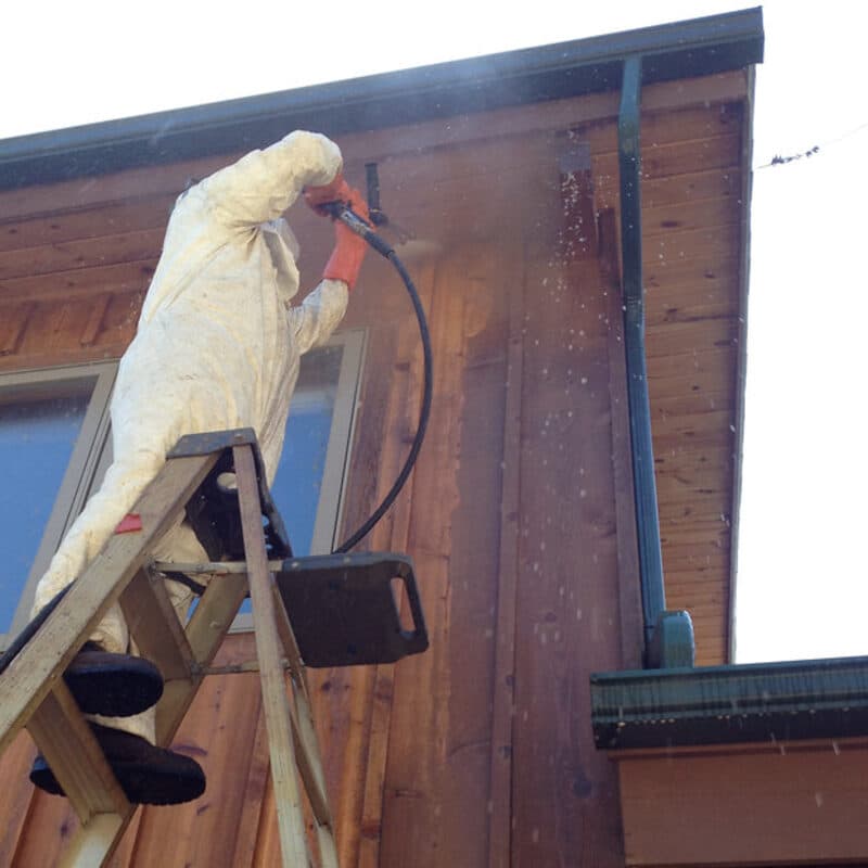Pressure washing old stain off wood siding from a ladder