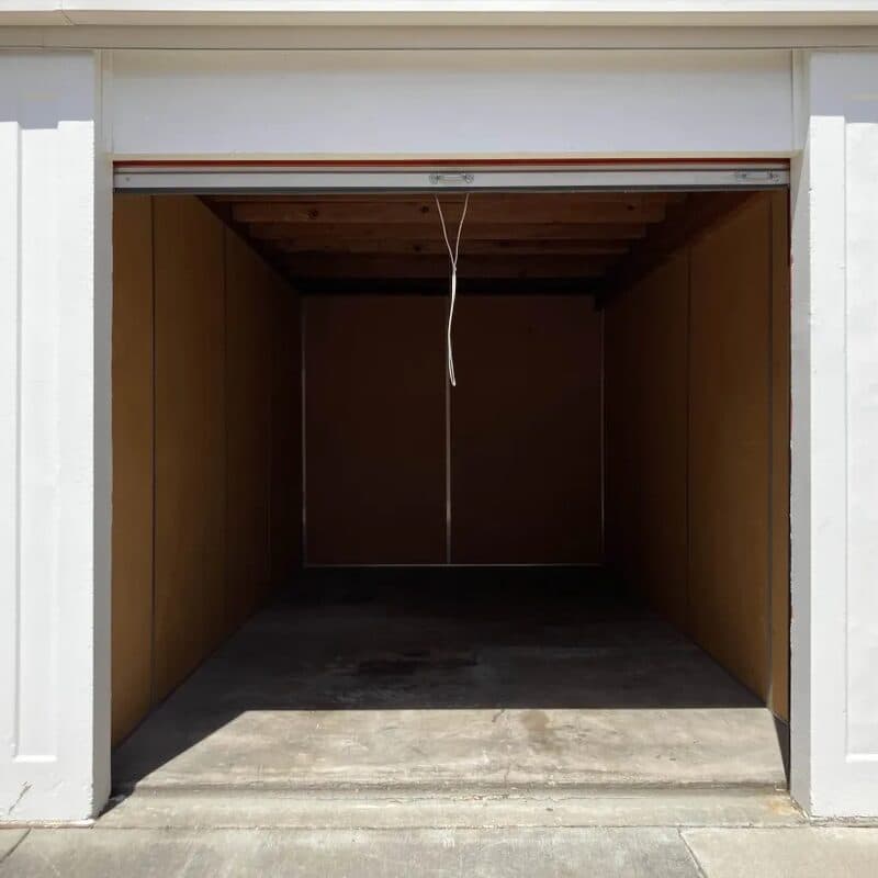 An empty storage unit with the roll-up door open and a bare concrete floor