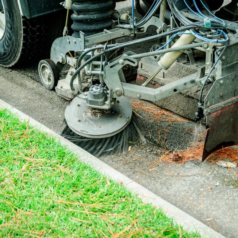 A street sweeper's gutter broom working along a curb line