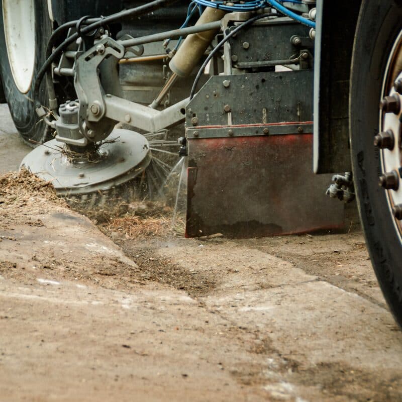 A sweeper's gutter broom pulling sand and pine needles off the pavement