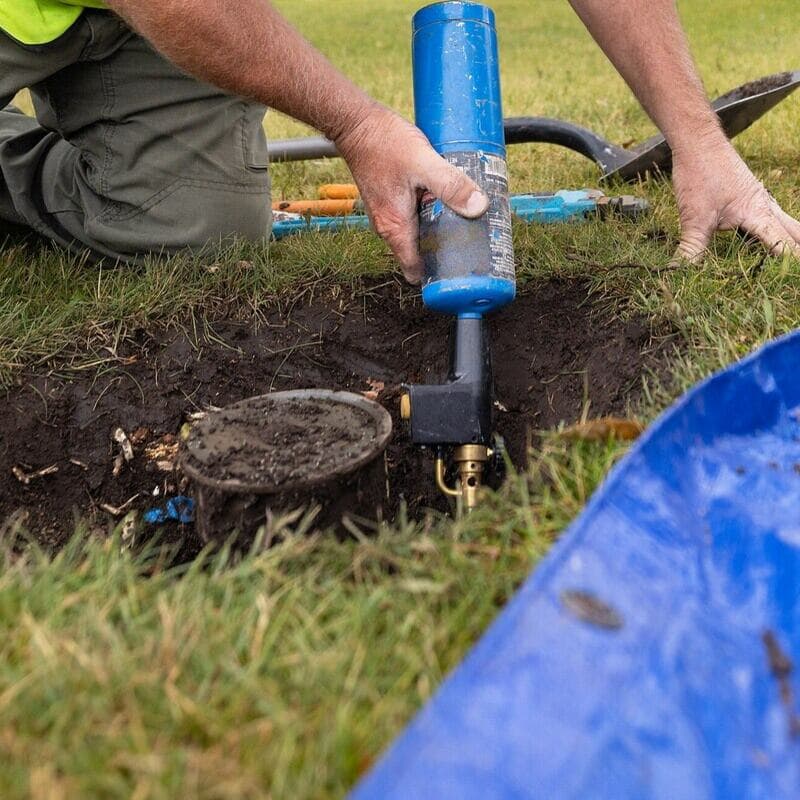 A torch held in the hole beside a sprinkler head during a repair