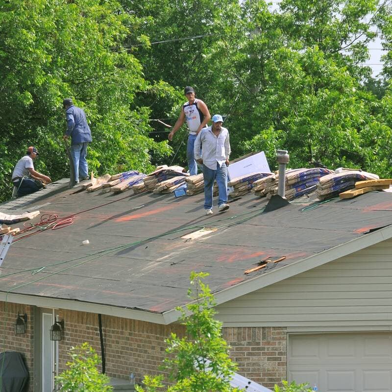 A crew on a roof with black underlayment down and shingle bundles staged along the ridge